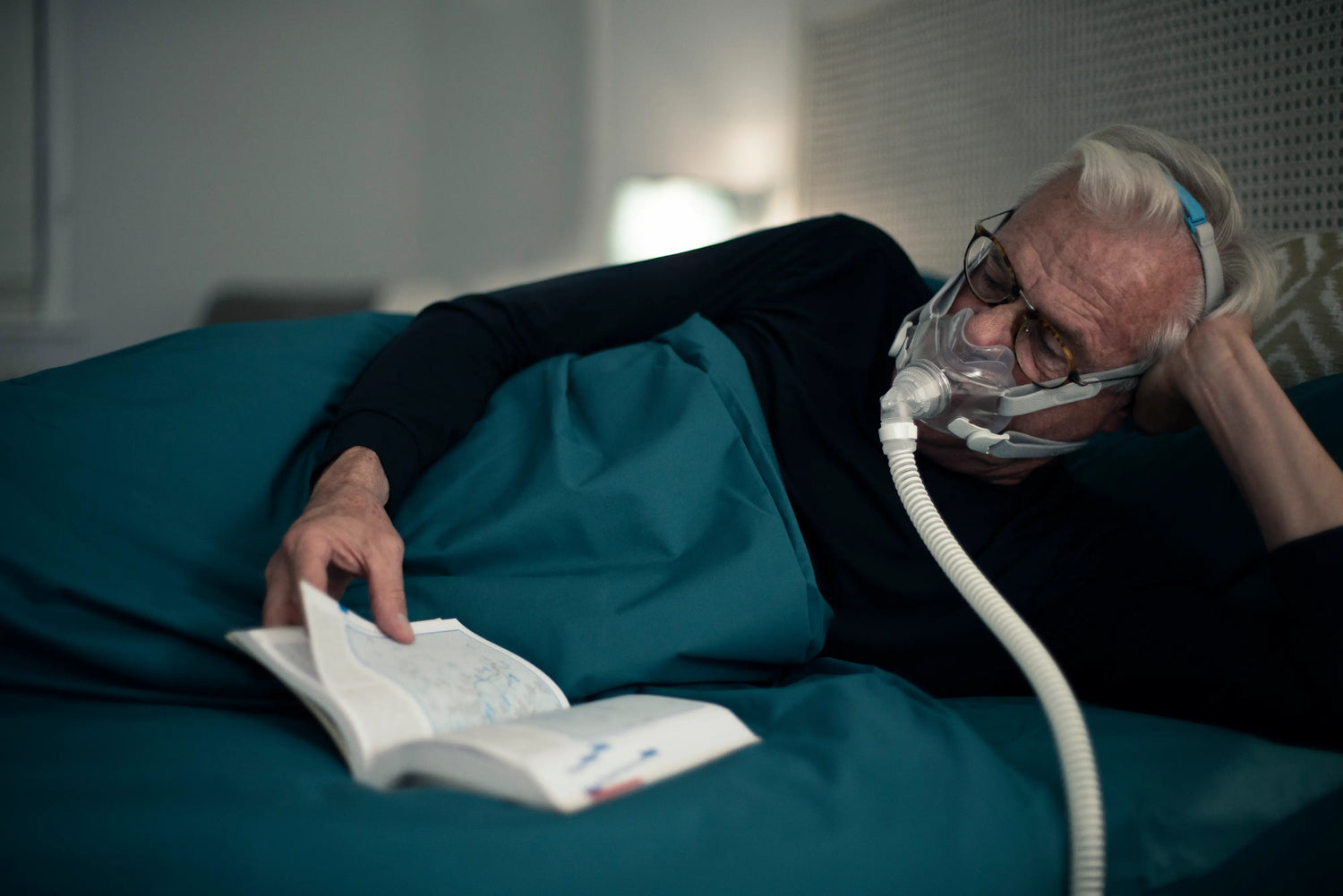 Man using cpap machine in bed while reading