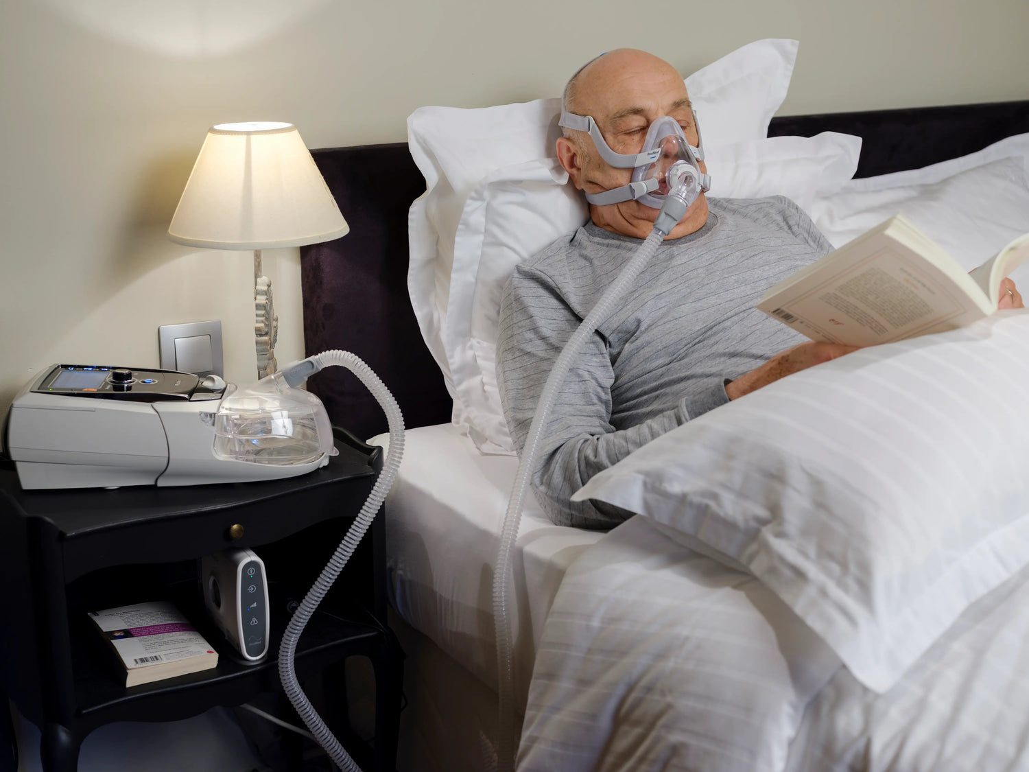 A man in bed using cpap mask while reading