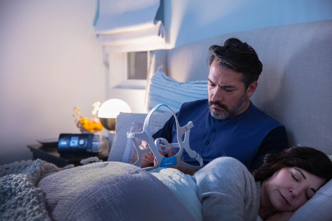 Husband checking his CPAP mask while wife is sleeping beside him
