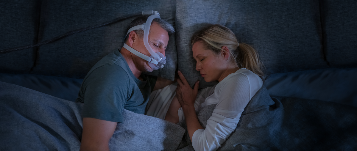 A man wearing the AirFit F30i Full Face CPAP Mask while sleeping with his wife beside him.