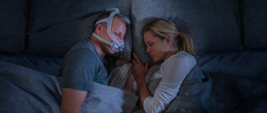 A man wearing the AirFit F30i Full Face CPAP Mask while sleeping with his wife beside him.