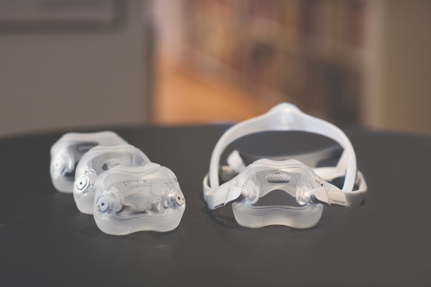 A clear plastic nasal pillow mask for CPAP therapy, with multiple sizes of the pillow component shown next to the headgear assembly.