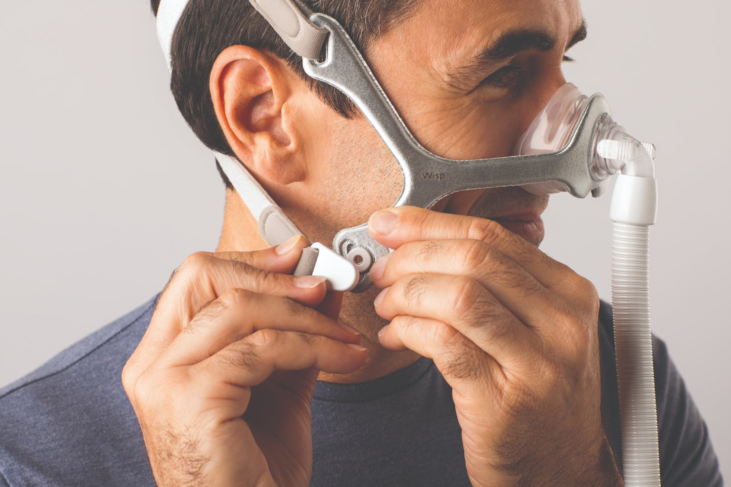 A man in the act of wearing the Wisp Nasal CPAP Mask